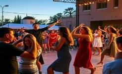 vibrant community participation, jubilant expression, performing arts, photorealistic, outdoor stage with audience, highly detailed, moving dancers, large aperture, bright contrasting colors, evening stage lighting, shot with a wide-angle lens.